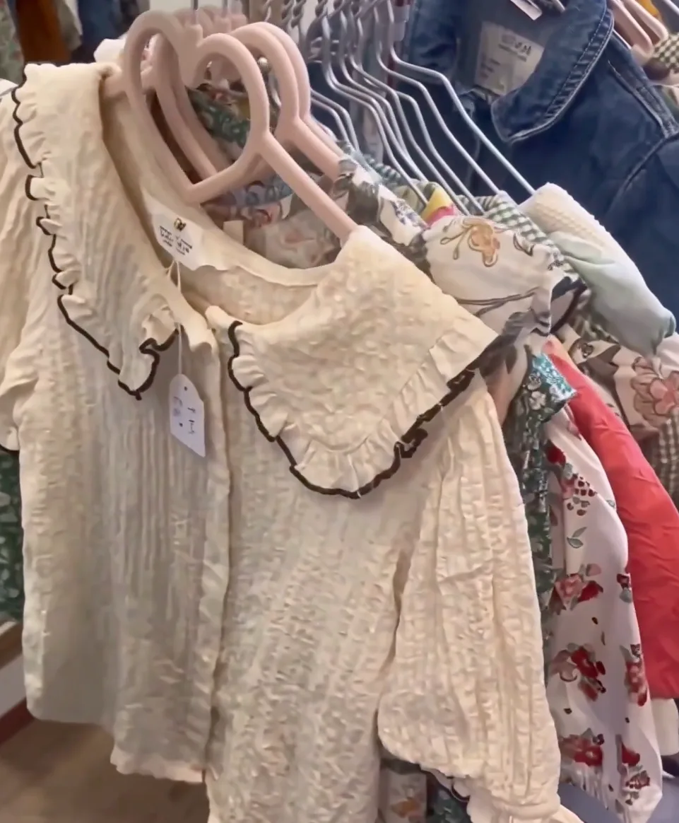 Blouses enfant beiges à col volanté sur cintres roses dans la boutique ColChic à Bourges